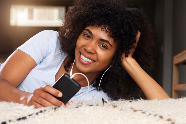 close-up-mulher-negra-em-casa-sorrindo-com-telefone-celular-e-fones-de-ouvido_33839-8812